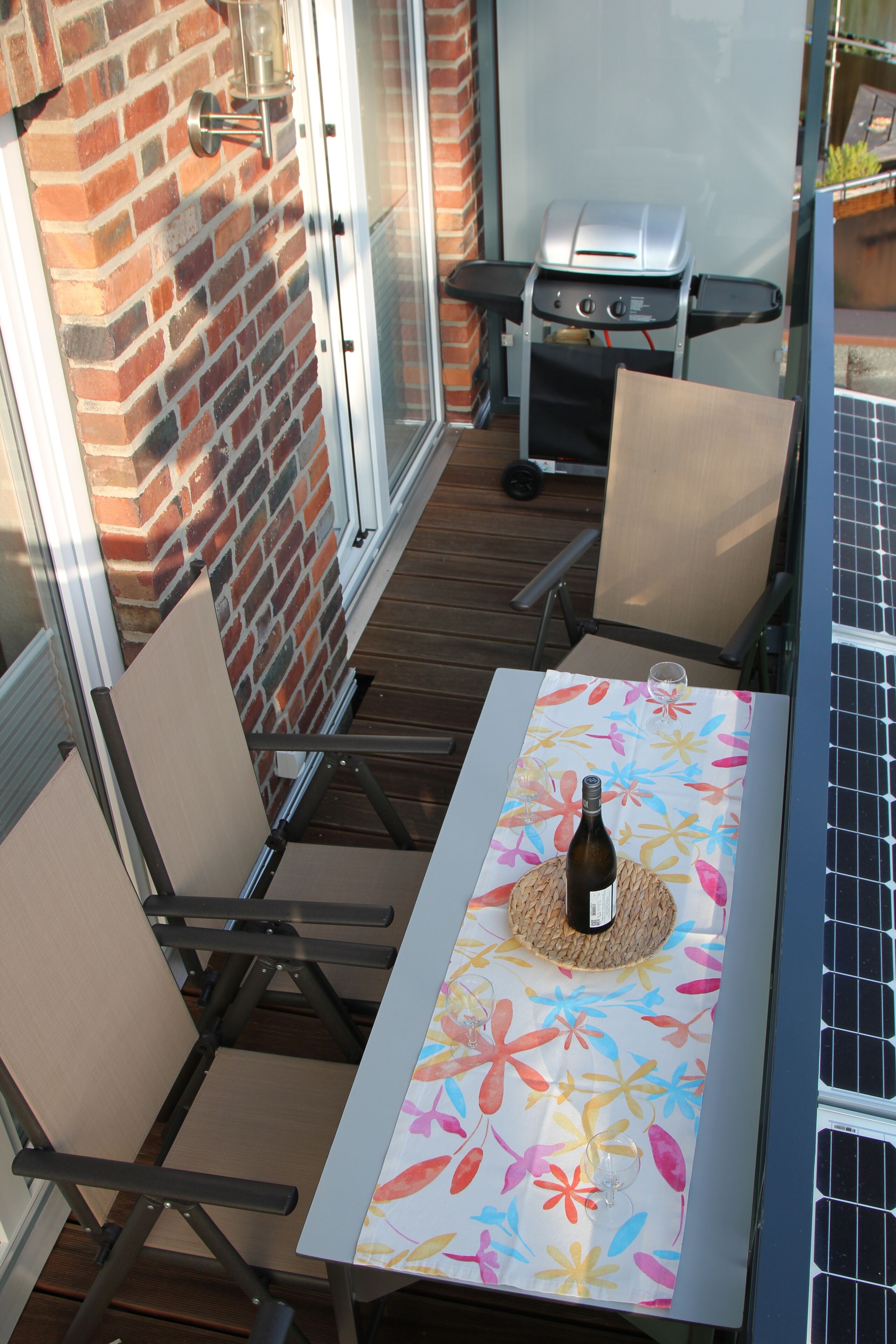 Eine Terrasse mit Tisch für zwei Personen, einem Grill und einer Solaranlage.