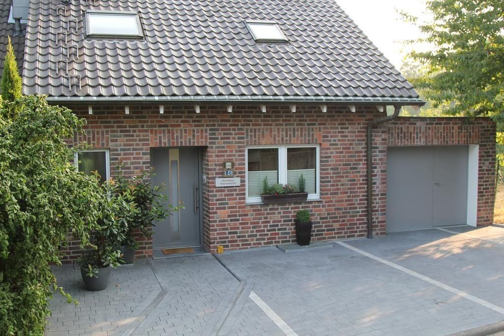 A two-story brick house with a tiled roof, a garage, and a small front garden with potted plants.