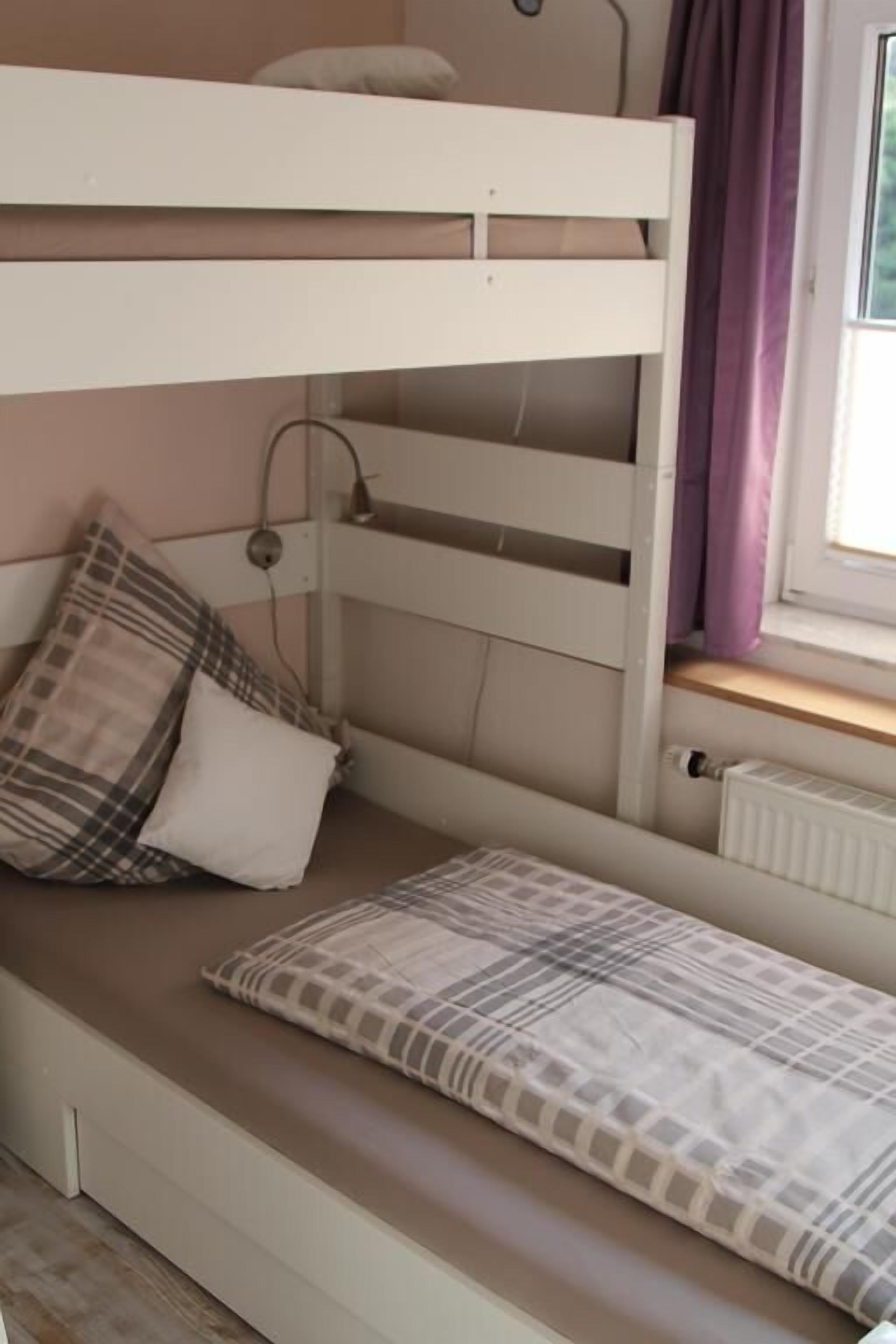 Un lit superposé avec un lit en bas et une tête de lit. Il y a des oreillers sur le lit du bas et une fenêtre avec des rideaux sur la droite.