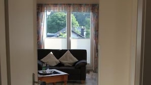 Ein Flur, der in ein Wohnzimmer mit einer Couch, einem Couchtisch und einem fenster mit Vorhängen führt.