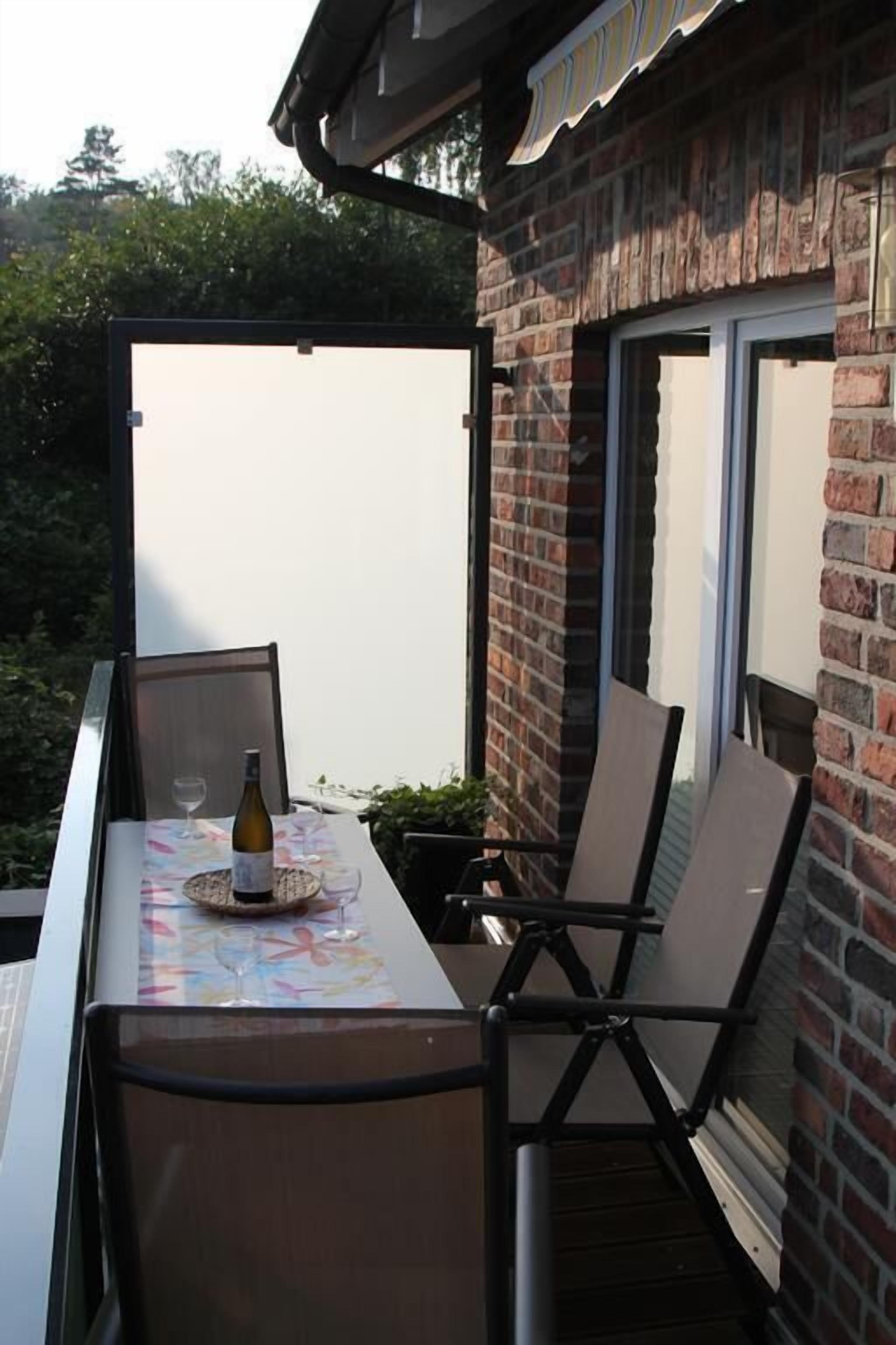 An outdoor patio with a table, chairs, a bottle, and a glass.