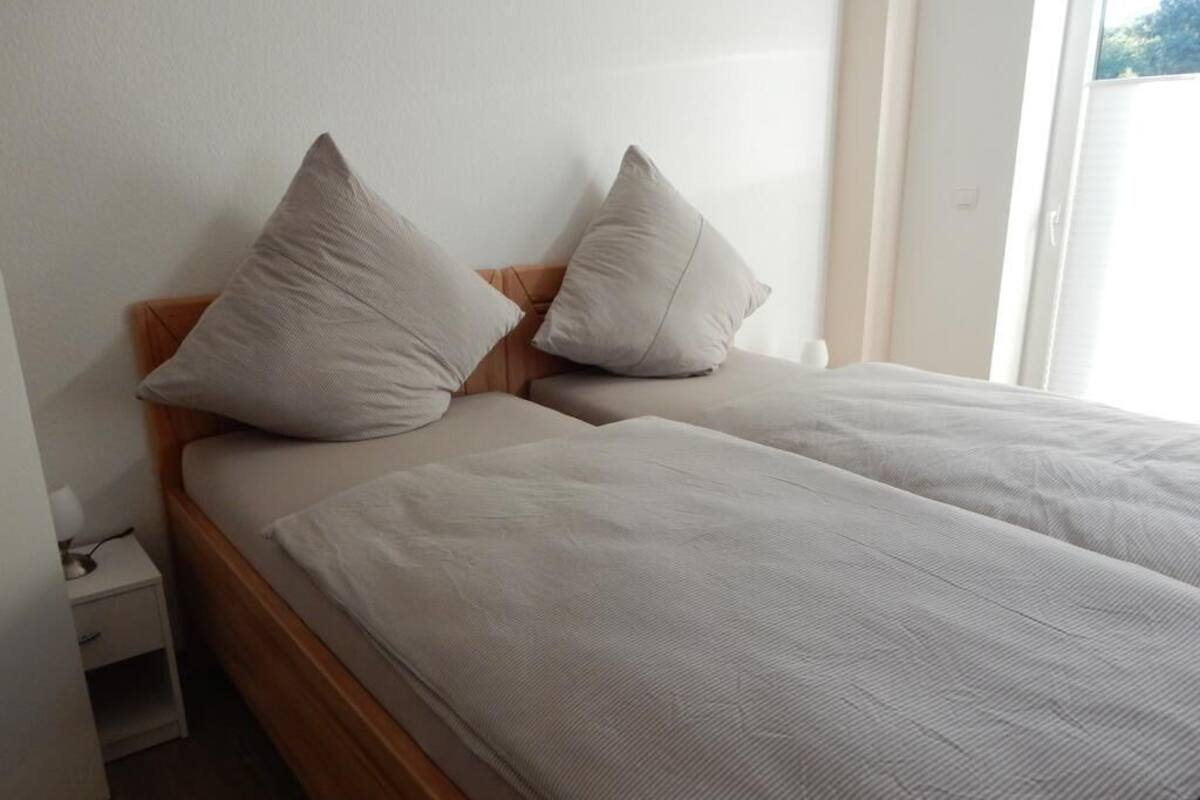 A double bed with two pillows, a wooden headboard, and a bedside table with a lamp.