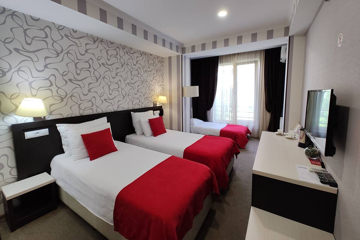 Una habitación de hotel con dos camas, un escritorio, un televisor y una ventana con cortinas.