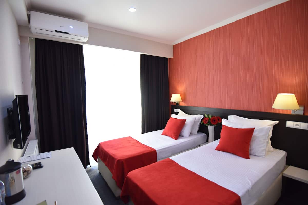 Una habitación de hotel con dos camas, ropa de cama roja y blanca, un escritorio con lámpara y un aire acondicionado.