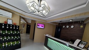 A hotel reception area with a modern design, including a reception desk, a wall-mounted television, and a decorative wall clock. - East Gate Boutique Hotel (Tbilisi)