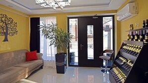 A living room with a sofa, a potted plant, a wine rack, and a door leading outside. - East Gate Boutique Hotel (Tbilisi)