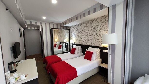 A hotel room with two beds, a desk, a TV, and a mirror. - East Gate Boutique Hotel (Tbilisi)
