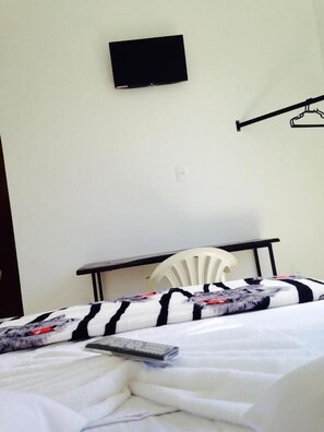 A simple room with a bed, a chair, a table, and a TV mounted on the wall.