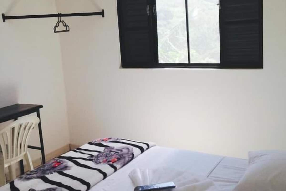 A bedroom with a bed, a desk, and a window with shutters.