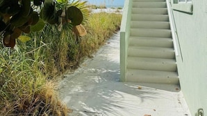 A concrete pathway leading to a white building with a window and a door. - 763 North Shore Upstairs 3 Bedroom Apts by RedAwning (Anna Maria)