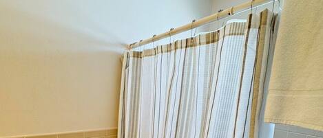 A bathroom with a toilet, two rolls of toilet paper, a shower curtain, and a towel hanging on the wall.