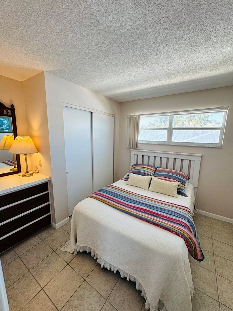 Een slaapkamer met een bed, een dressoir, een raam en een plafondventilator.