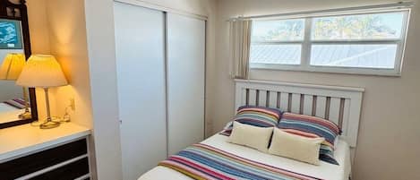 Een slaapkamer met een bed, een dressoir, een raam en een plafondventilator.