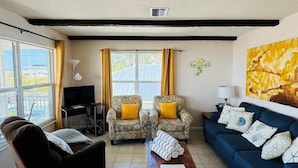 A living room with a black sofa, a blue sofa, a wooden coffee table, two armchairs with yellow cushions, and a TV on a stand. - 763 North Shore Upstairs 3 Bedroom Apts by RedAwning (Anna Maria)