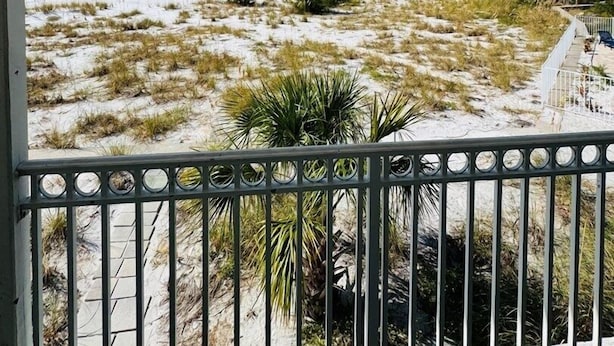 A balcony with a view of a sandy beach with sparse vegetation and a clear sky. - 763 North Shore Upstairs 3 Bedroom Apts by RedAwning (Anna Maria)