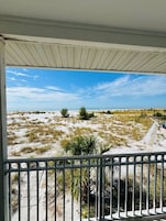A balcony with a view of a sandy beach with sparse vegetation and a clear sky.
