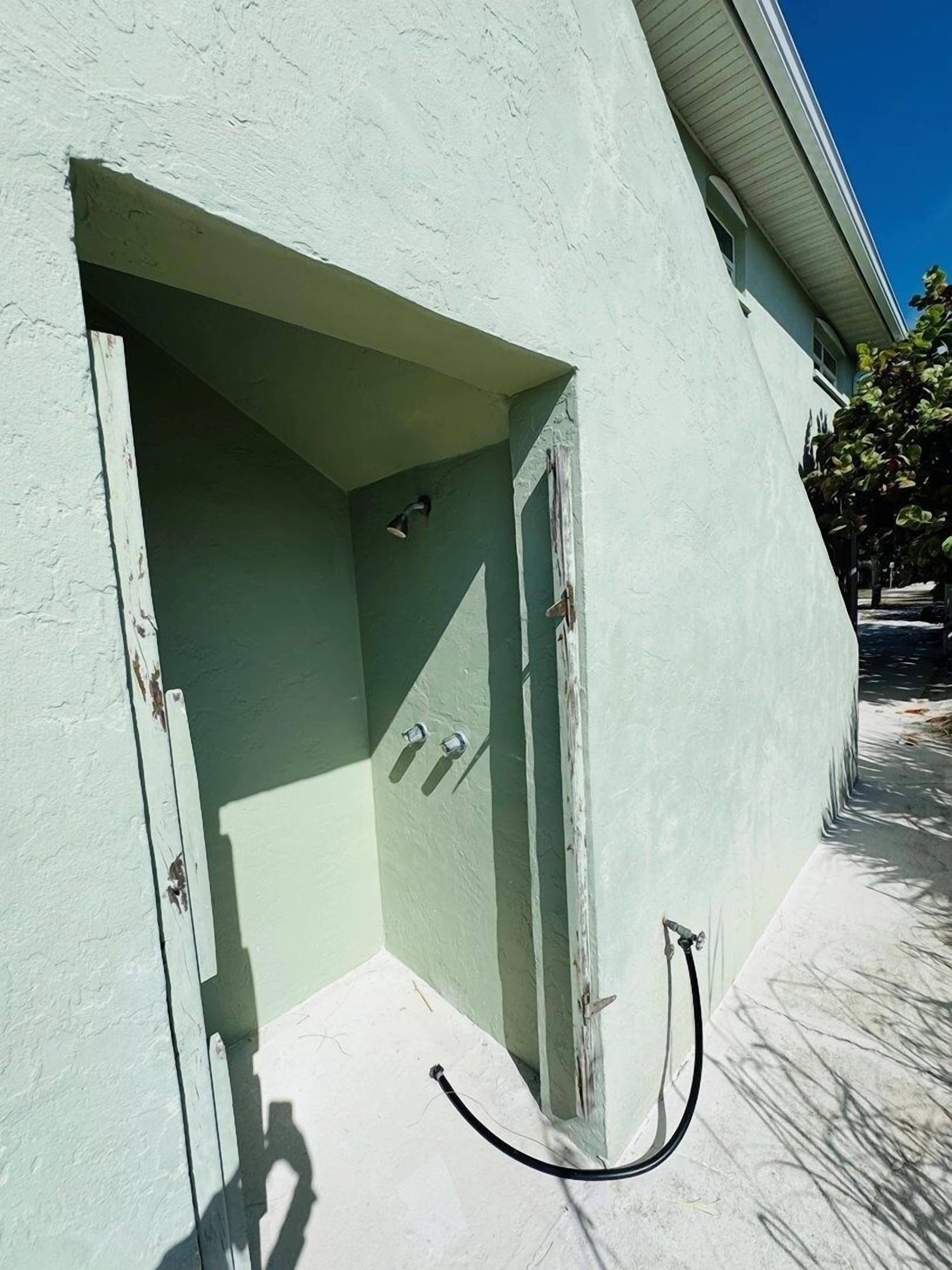 Un bâtiment doté d’une façade verdoyante, d’une petite entrée avec une porte et d’une prise électrique visible.