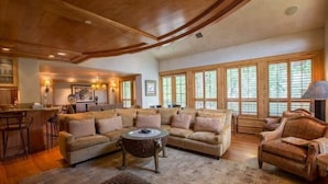 A spacious living room with a large sectional sofa, a coffee table, and a fireplace. There are large windows providing natural light and a view of the outdoors. - Northwoods Luxury Condo Close to Chairlift by RedAwning (Vail)