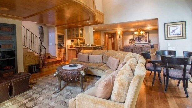 A spacious living area with a large sectional sofa, a dining table with chairs, a staircase, and a kitchen in the background. - Northwoods Luxury Condo Close to Chairlift by RedAwning (Vail)