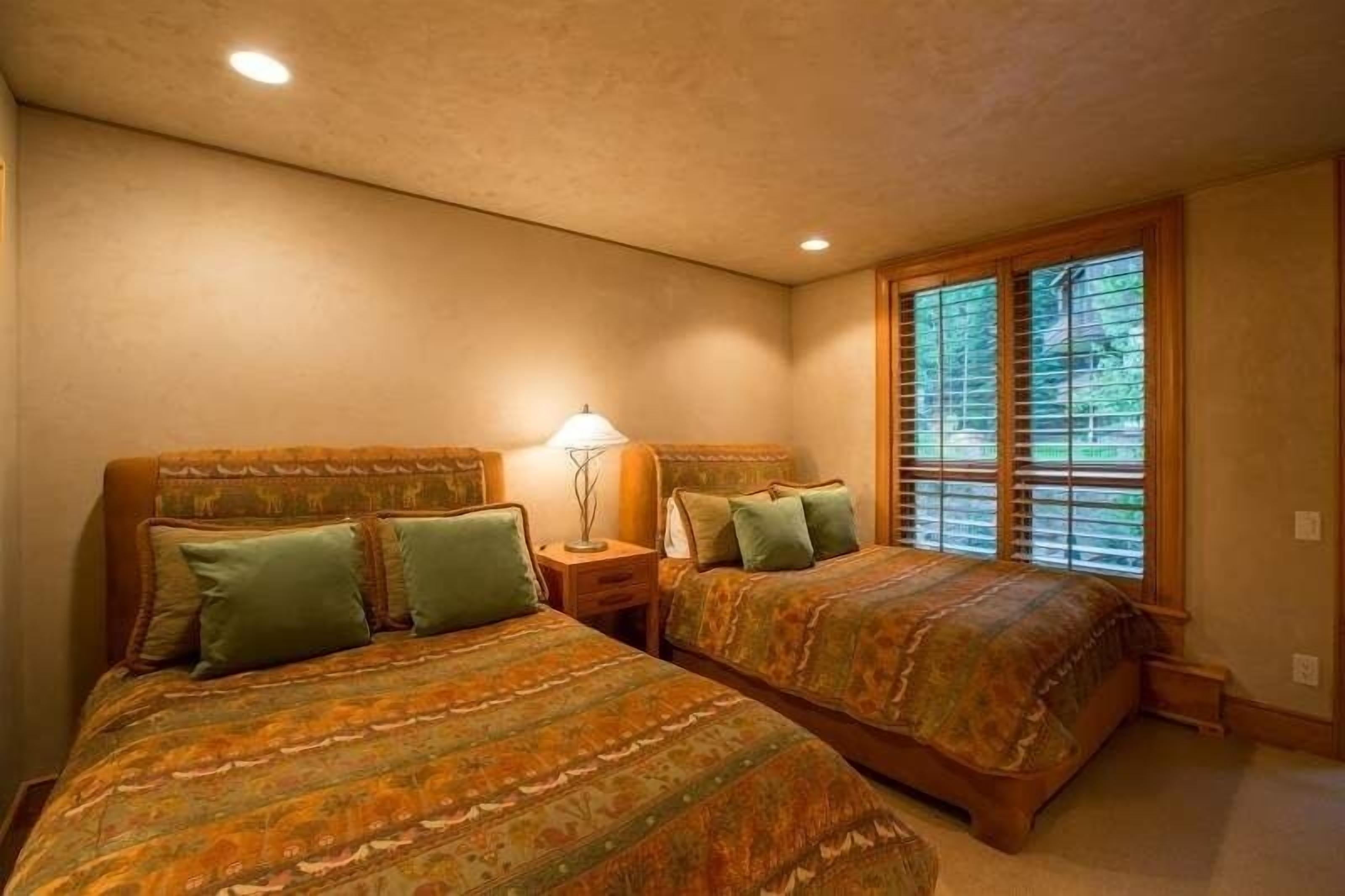A bedroom with two beds, a nightstand, a lamp, and a window with blinds.