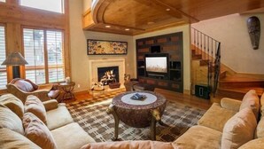 A spacious living room with a fireplace, a large window, and a staircase. - Northwoods Luxury Condo Close to Chairlift by RedAwning (Vail)
