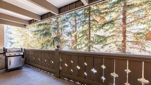 A balcony with a view of tall trees, a grill, and a wooden railing with decorative elements. - Villa Cortina Condo 5 Minutes Walk to Vail Village by RedAwning (Vail)