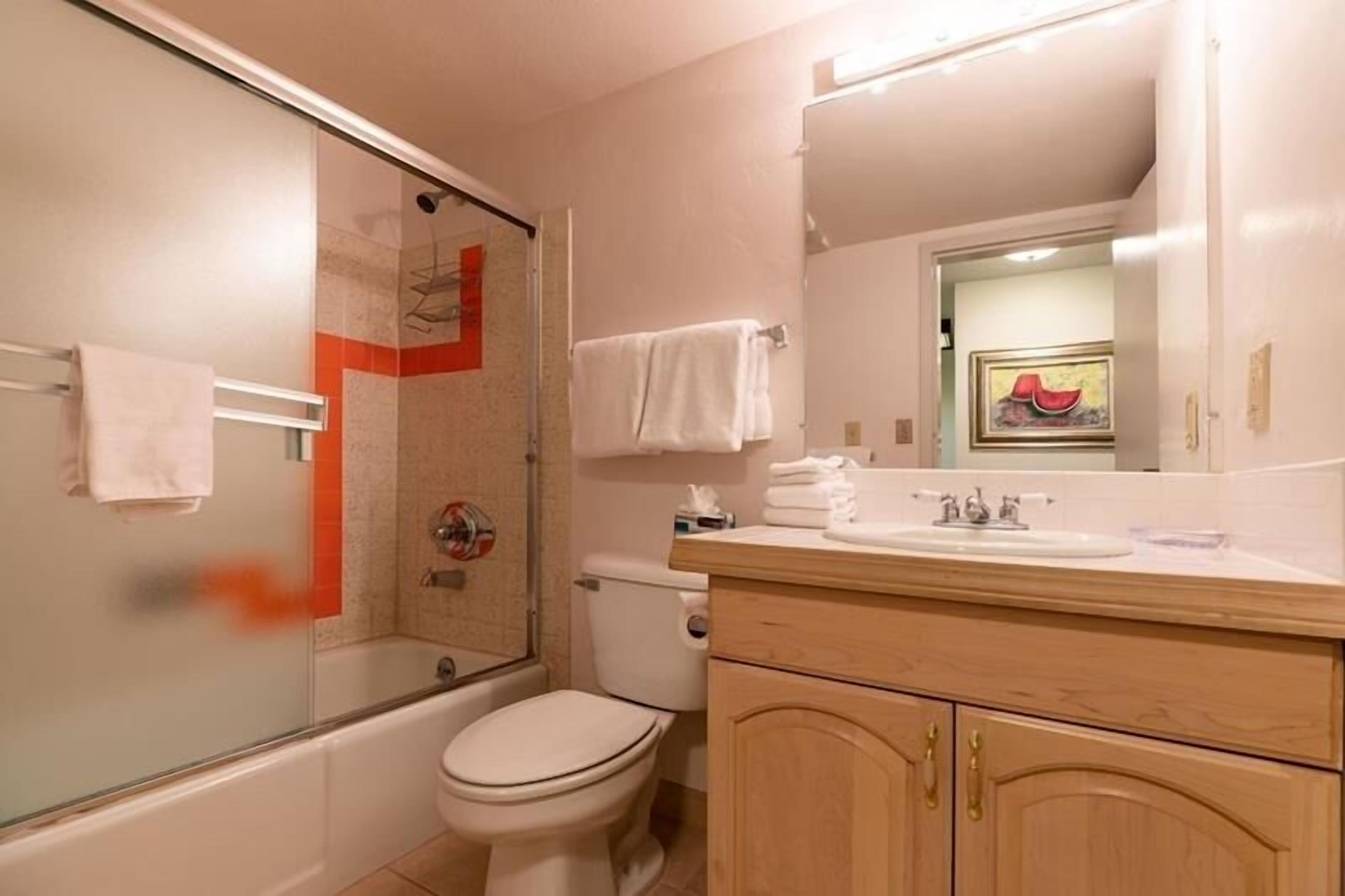 A bathroom with a glass shower enclosure, a toilet, a sink with a mirror, and wooden cabinets.