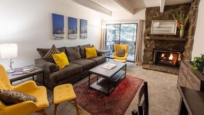 A living room with a fireplace, a sofa, a coffee table, and a yellow armchair. - Villa Cortina Condo 5 Minutes Walk to Vail Village by RedAwning (Vail)