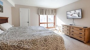 A bedroom with a large bed, a wooden dresser, a television on the wall, and a window with a view of buildings. - Breakaway West Ski Condo 1,5 miles from the Lifts by RedAwning (Vail)