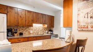 A kitchen with wooden cabinets, a granite countertop, and a dining area with two chairs. - Breakaway West Ski Condo 1,5 miles from the Lifts by RedAwning (Vail)