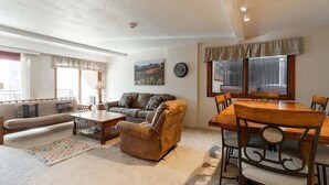 A living room with a sofa, armchair, coffee table, and dining table with chairs. There is a clock on the wall and a window with curtains. - Breakaway West Ski Condo 1,5 miles from the Lifts by RedAwning (Vail)