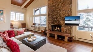 Una sala de estar acogedora con una chimenea de piedra, un ventanal con vistas a árboles cubiertos de nieve y un área de descanso confortable.
