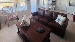 A living room with a brown leather couch, a wooden coffee table, and a dining area with white chairs. - 763 North Shore Downstairs 3 Bedroom Apts by RedAwning (Anna Maria)