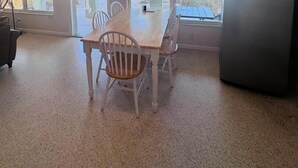 A room with a dining table, chairs, a refrigerator, and a view of the beach through a window. - 763 North Shore Downstairs 3 Bedroom Apts by RedAwning (Anna Maria)