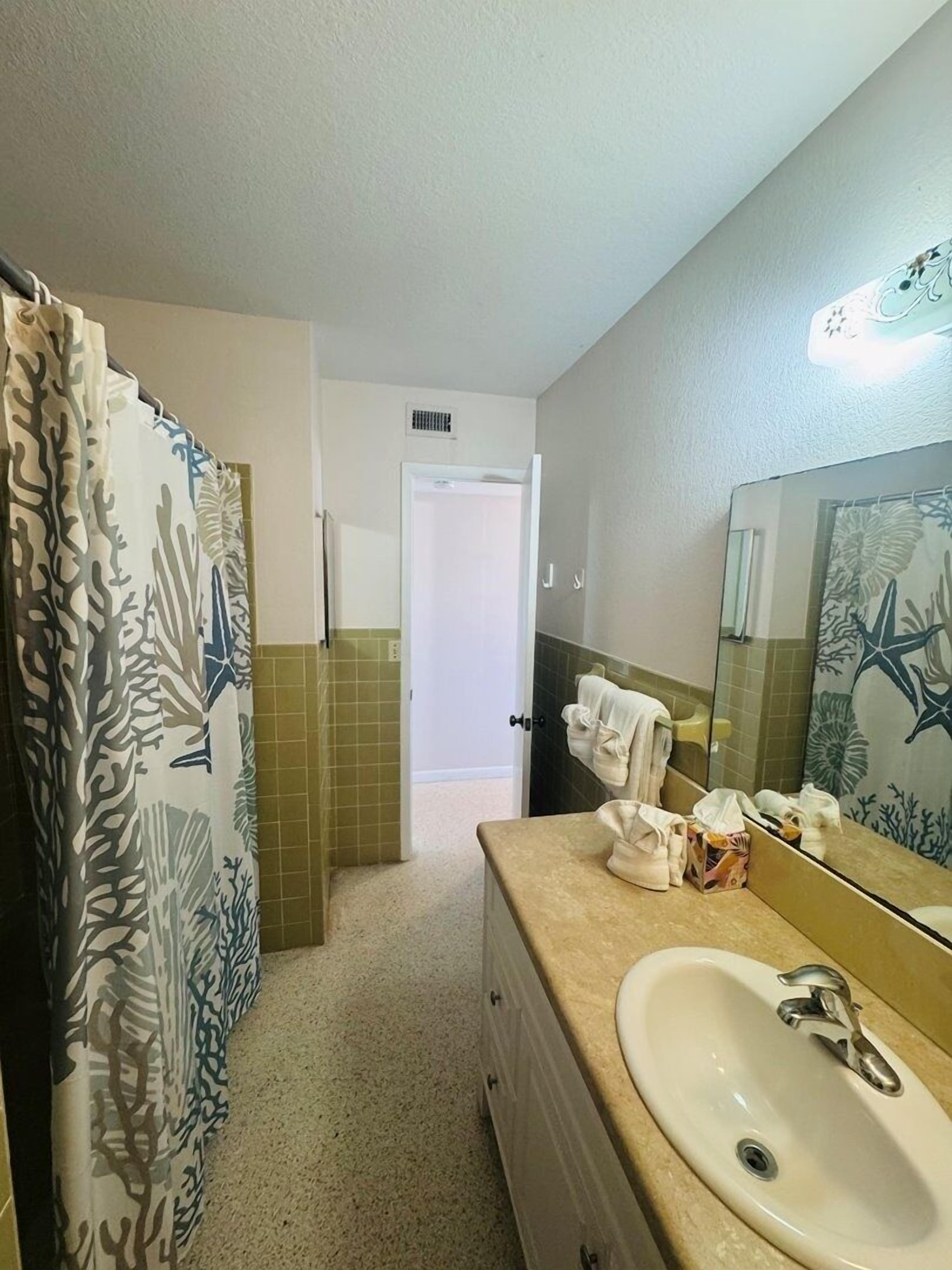 A bathroom with a sink, mirror, shower curtain, and towels.