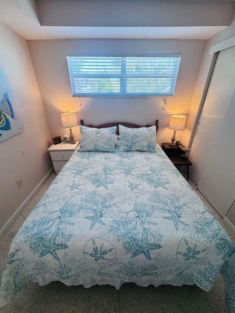 Une chambre à coucher avec un lit, deux tables de chevet, une fenêtre et une lampe fixée au mur.