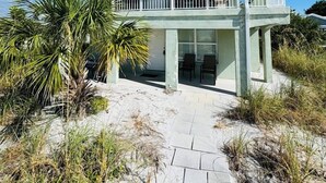 A two-story beachfront house with a balcony, surrounded by beach vegetation. - 763 North Shore Downstairs 3 Bedroom Apts by RedAwning (Anna Maria)