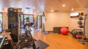 Ein Fitnessstudio mit Trainingsgeräten, Laufband und einem an der Wand montierten Fernseher.