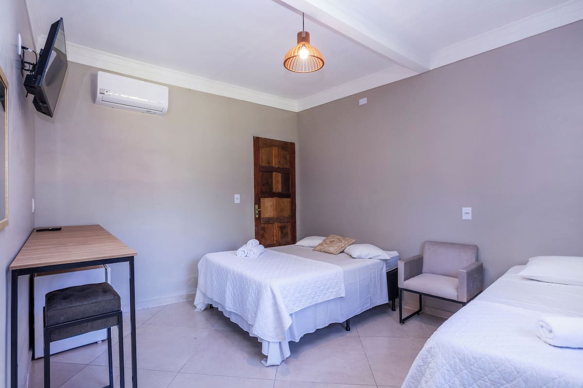 A hotel room with two beds, a desk, a chair, an air conditioning unit, and a television.