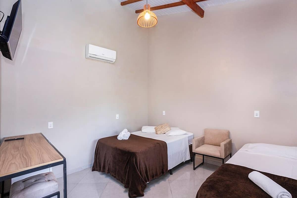 A small, well-lit room with two beds, a chair, a desk, and a TV.
