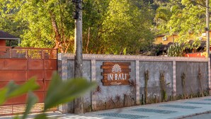 A sign reading "IN BALI Village" with a decorative emblem, surrounded by greenery and a paved area. - Pousada In Bali (São Sebastião)