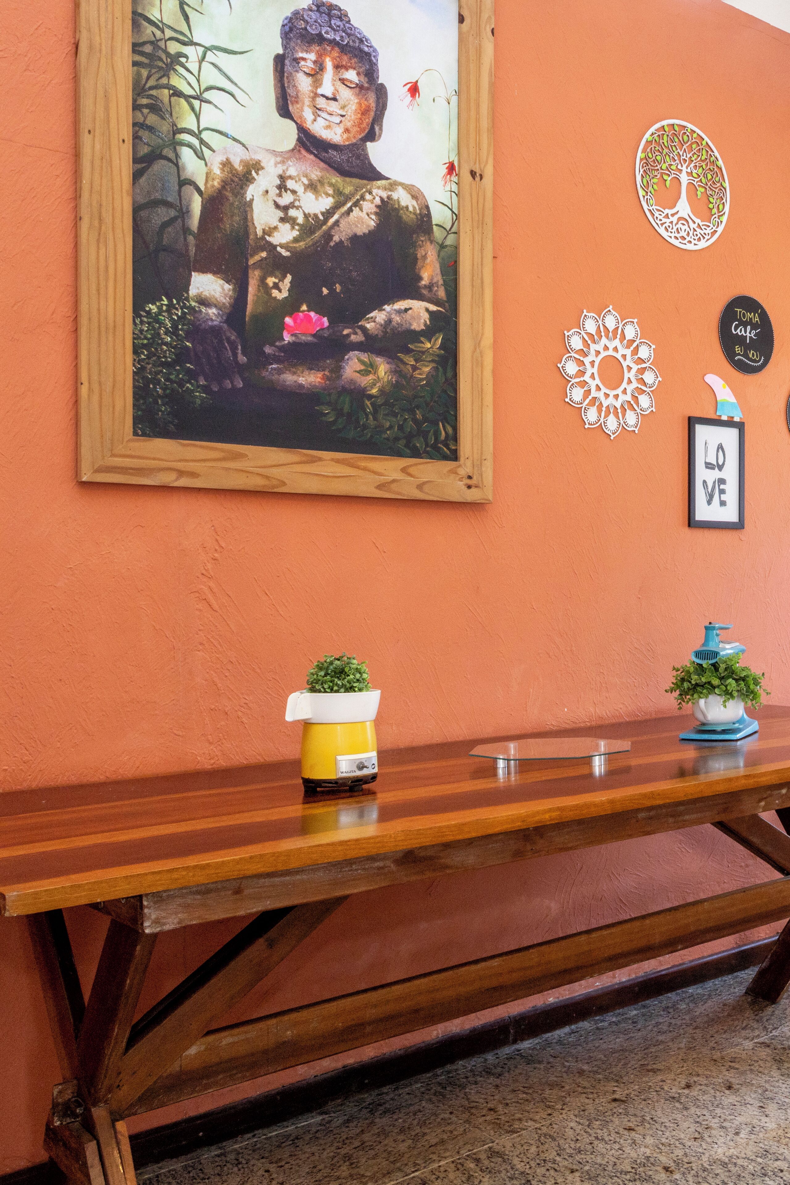 A wooden bench with potted plants and a Buddha statue on the wall.