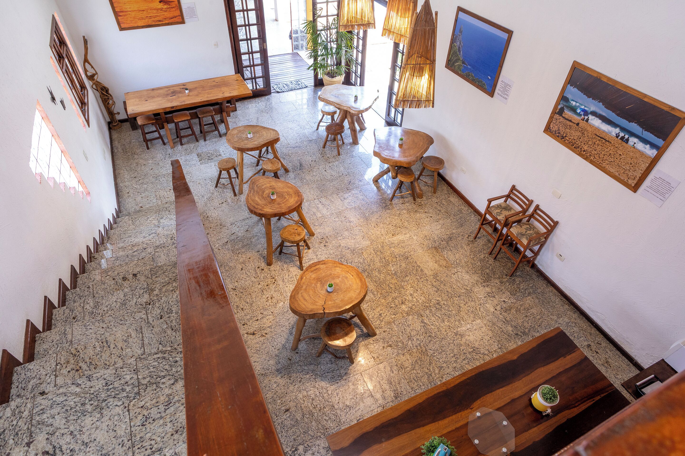 Un espacio amplio con una mesa de madera central rodeada de sillas, una escalera que lleva a un nivel superior y vista a la playa a través del espacio abierto.
