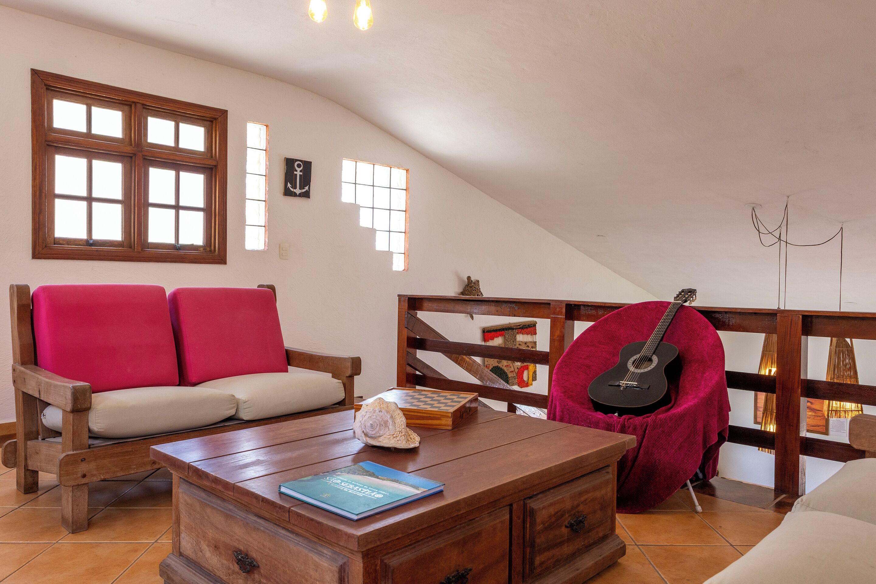 Una stanza accogliente con un divano in legno, un tavolino da caffè con un libro, una chitarra e vista all'esterno da una finestra.