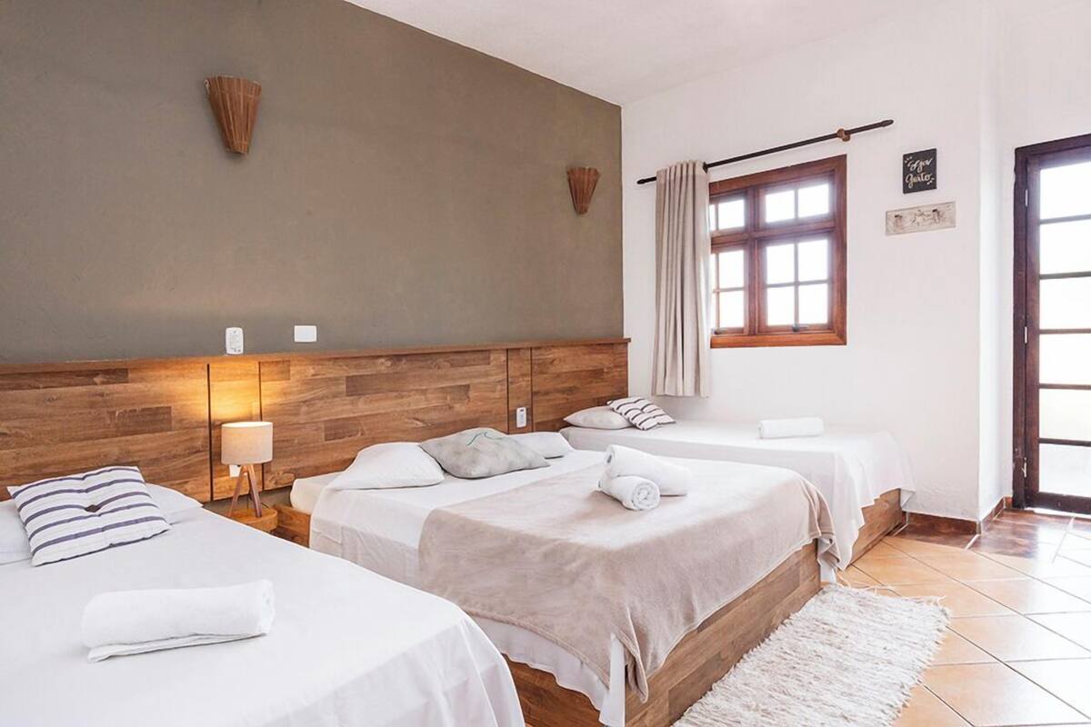 A hotel room with two beds, a wooden headboard, a window with curtains, and a wall-mounted lamp.