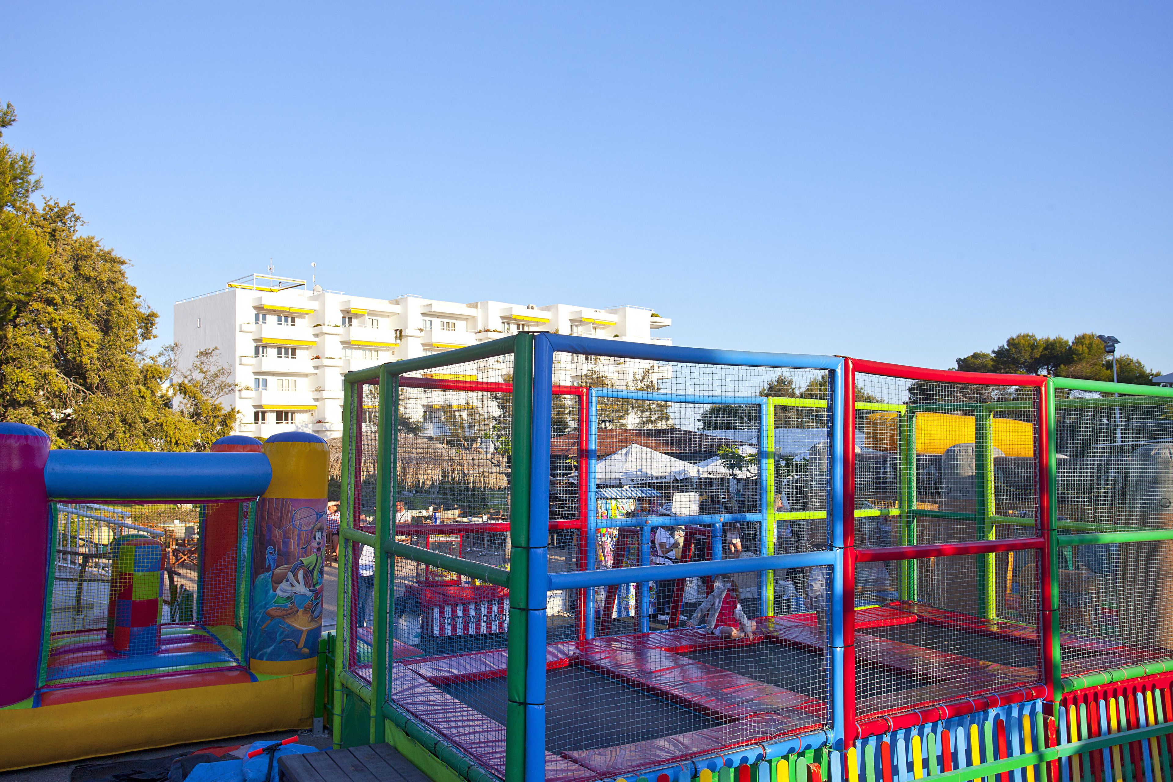 Ein farbenfroher Spielbereich mit Netzumrandung, Rutsche und Trampolin.