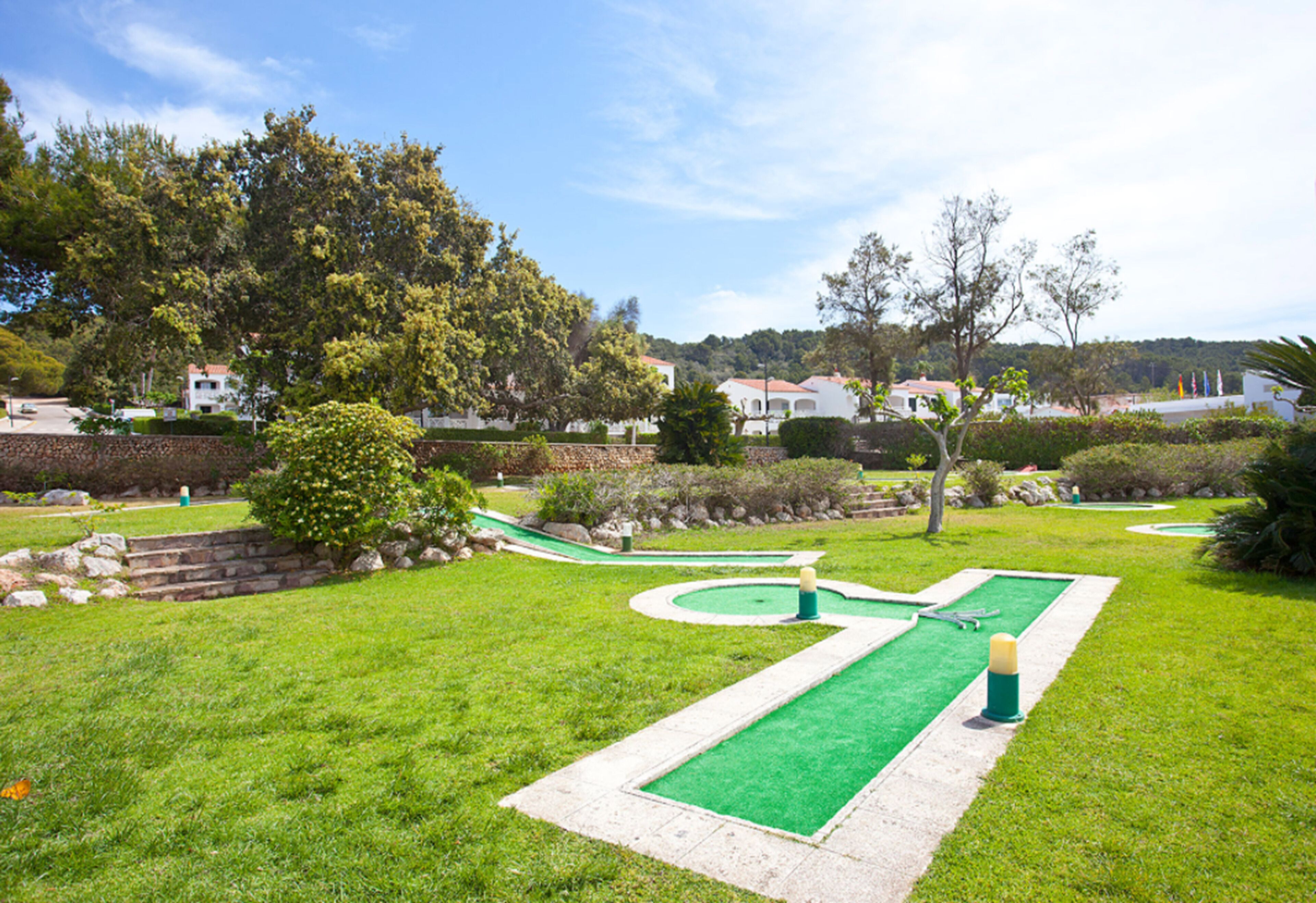Un campo de golf con un putting green, rodeado de césped y árboles bien cuidados.