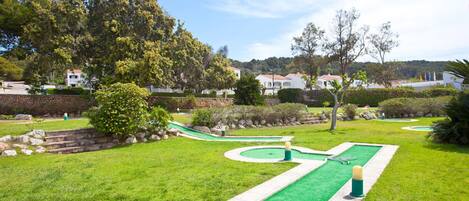 Un campo de golf con un putting green, rodeado de césped y árboles bien cuidados.