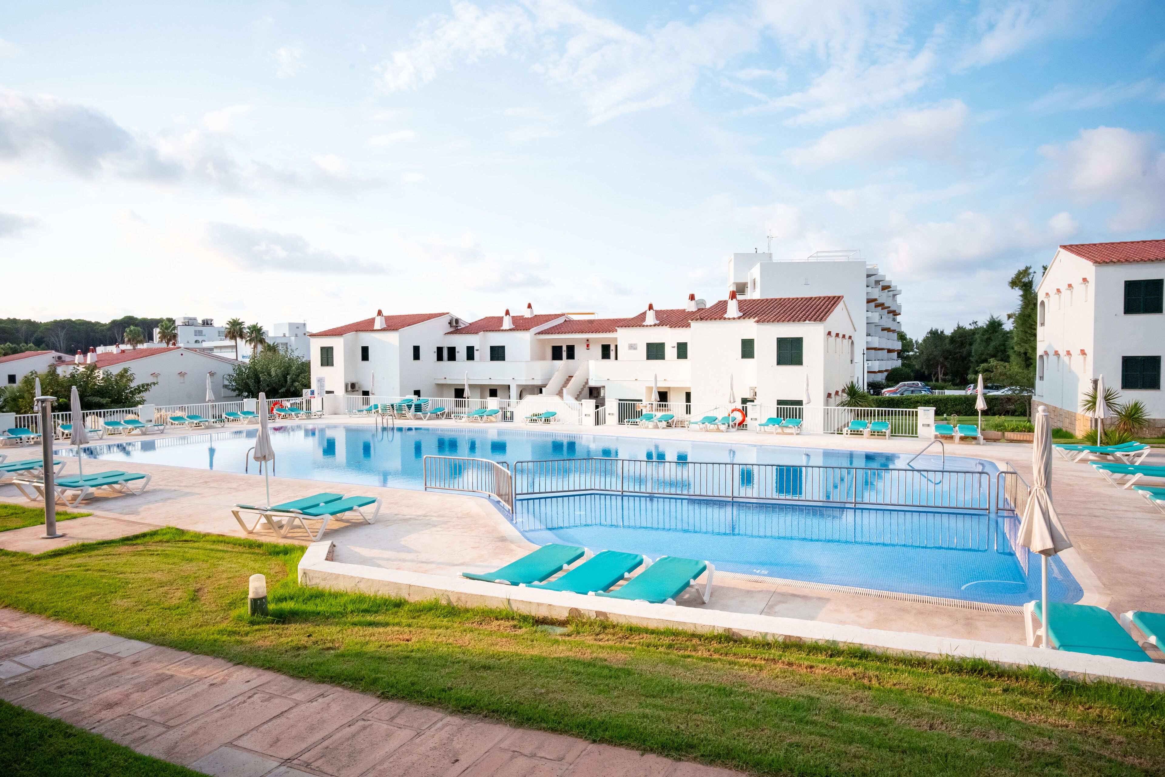 A swimming pool with lounge chairs, a building with red-tiled roofs, and a clear sky.