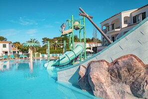 Una piscina con tobogán de agua, sillas de descanso y un edificio con balcones al fondo.